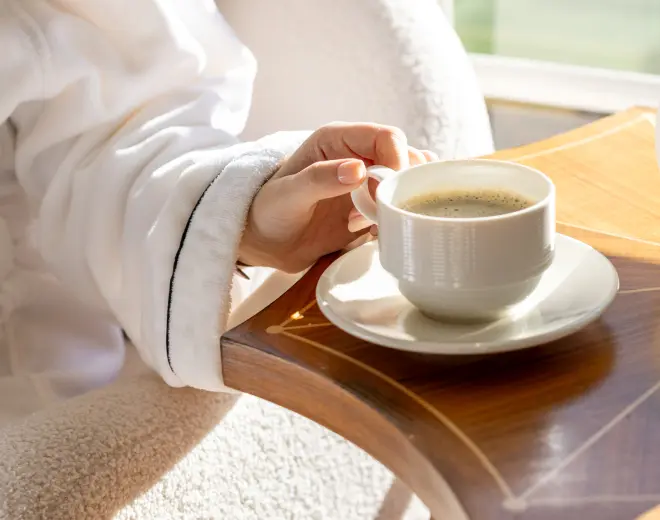 A guest holding his cup of coffee in the room with a bathrobe during in-room dining.